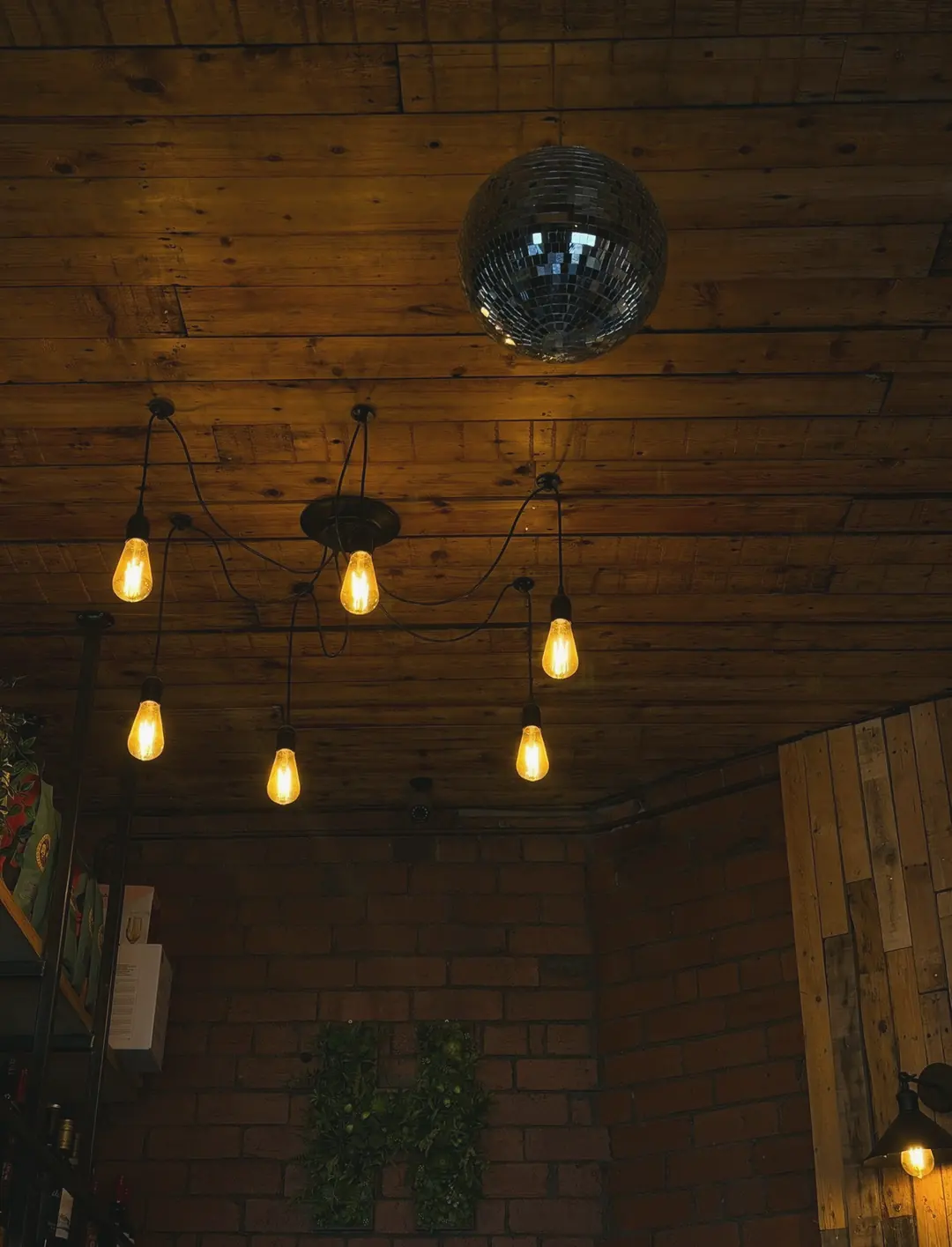 Bulb lights on long black flexes and a disco ball hanging from the wooden ceiling, above a brick wall