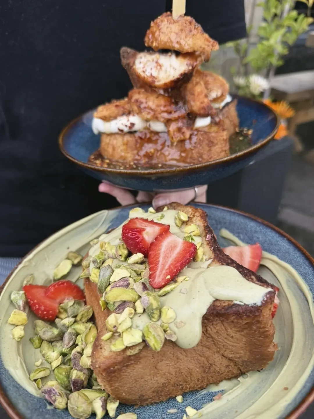 Pistachio French toast with strawberries and crushed pistachios, and a stack of French toast with fried chicken behind