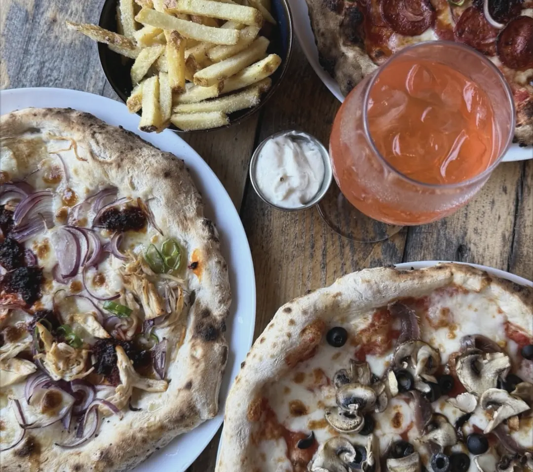 Three pizzas from above with fries, a dip and an orange spritz